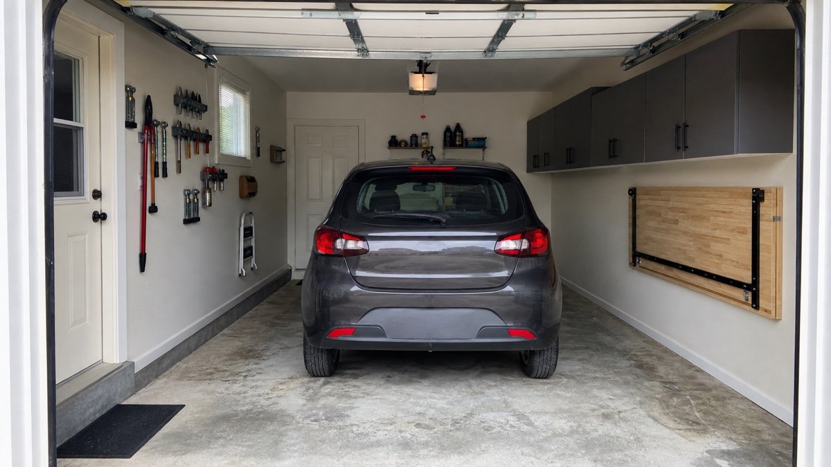 Car parked in a narrow garage with a wall mounted workbench folded flat beside it