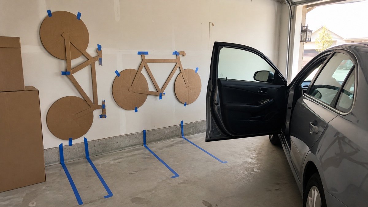 Cardboard bike outlines taped on a garage wall beside a parked car